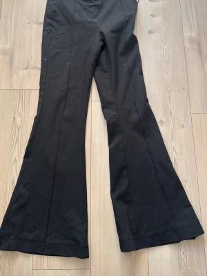 Svarta utsvängda kostymbyxor - Snygga svarta kostymbyxor med utsvängda ben och pressveck. Perfekta för dig som vill ha en stilren och trendig look. Byxorna har en klassisk passform och är tillverkade i ett mjukt material som ger en bekväm känsla hela dagen.