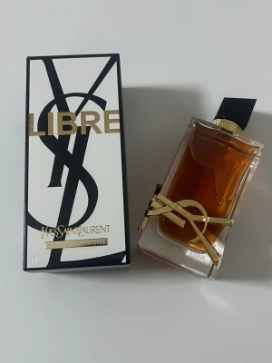 Yves Saint Laurent Libre Intense 90ml - YSL Libre Intense är en lyxig parfym i en elegant, rektangulär glasflaska med guldiga detaljer och svart kork. Doften kommer i en vit och svart kartong med guldtext. Flaskan rymmer 90 ml och har en exklusiv design med YSL-loggan i metall.