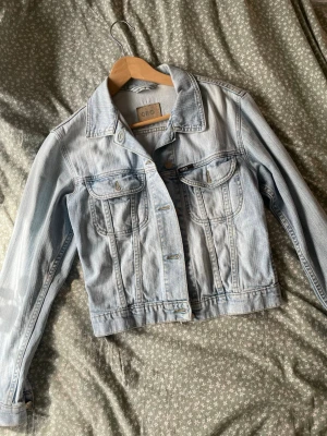 Ljusblå jeansjacka  - Snygg ljusblå jeansjacka från Gina Tricot med klassisk krage, bröstfickor med lock och knappstängning framtill. Jackan har en rak, kortare passform och är tillverkad i denim med tydliga sömmar. Perfekt för en trendig och avslappnad look.