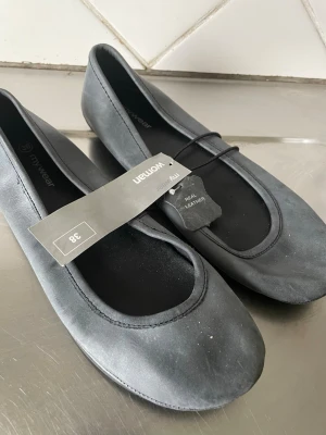 Mörkgråa ballerinaskor i läder - Stilrena mörkgrå ballerinaskor från Mywear i äkta läder. Skorna har rund tå och klassisk design med låg klack. Perfekta för dig som gillar enkel och tidlös stil. Märkta med 'real leather' och har en mjuk innersula för extra komfort.