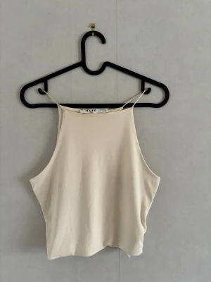 Cremevit linnetopp från NA-KD - Snygg beige linnetopp från NA-KD med tunna axelband och rak halsringning. Toppen är ärmlös och har en enkel, stilren design som passar perfekt till sommaren. Tillverkad i mjukt material för en bekväm känsla. Aldrig använd och i helt nyskick! Ny pris på hemsidan 91 kr