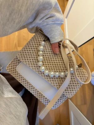 Beige vävd handväska med pärldetalj - Superfin väska, köpt på Rhodos. Nyskick!! Pärldetaljen går att ta av!