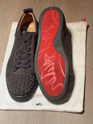 Christian Louboutin grå ni får mer 3 extra spikar i köpet - Svarta sneakers från Christian Louboutin med klassisk röd sula och nitar på tån. Skorna har lågt skaft, svarta skosnören och är tillverkade i läder och textil. Perfekt för dig som vill sticka ut med exklusiv design och edgy detaljer.
