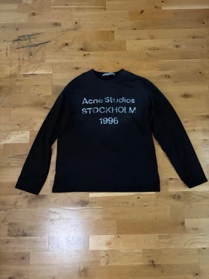 Svart långärmad tröja Acne Studios - Svart långärmad tröja från Acne Studios med tryck 'Acne Studios STOCKHOLM 1996' på bröstet. Tröjan har rund hals och är tillverkad i ett mjukt material som passar perfekt för en avslappnad och cool look.