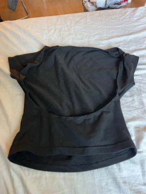 Svart croppad topp med öppen rygg - En enkel svart croppad topp med korta ärmar och rund hals. Perfekt till jeans eller kjol för en clean och stilren look. Tillverkad i mjukt material som känns skönt mot huden.Och har öppen rygg