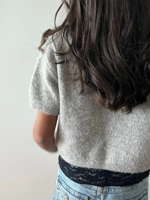 Ljusgrå stickad kortärmad tröja - Mysig ljusgrå stickad tröja med korta ärmar och rund halsringning. Tröjan har en enkel och stilren design, perfekt att matcha med jeans eller kjol. Materialet ser ut att vara en mjuk ull- eller ullblandning. Inga synliga loggor eller märken.