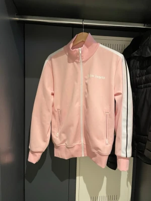 Rosa track jacket från Palm Angels - Säljer en snygg rosa track jacket från Palm Angels med vita och svarta ränder längs ärmarna. Den har lite tvättfläckar annars är den perfekt 