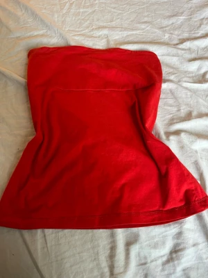 Röd tubtopp från Gina Tricot - Snygg röd tubtopp från Gina Tricot i mjuk bomull. Enkel och stilren modell utan axelband, perfekt att matcha med jeans eller kjol. Toppen har en klassisk bandeau-form och är superbekväm att bära.