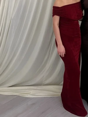 Vinröd offshoulder långklänning - Snygg vinröd långklänning med offshoulder-design och draperade detaljer upptill. Klänningen har en figurnära passform och är tillverkad i ett mjukt, stretchigt material som ger en elegant siluett. Perfekt för dig som vill sticka ut med stil. Använd endast 1 gång