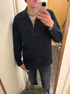Mörkblå overshirt från Tresanti - Stilren mörkblå overshirt från Tresanti med klassisk krage och knäppning framtill. Två bröstfickor med lock ger en snygg och praktisk look. Perfekt att bära över en tröja för en avslappnad men uppklädd stil.