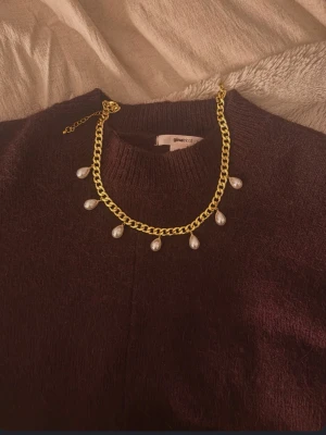 Guldfärgat halsband med pärlor - Snyggt halsband med kraftig guldfärgad kedja och droppformade vita pärlor som hänger längs kedjan. Halsbandet har justerbar längd och ger en trendig och elegant look. Perfekt accessoar för att lyfta din outfit.