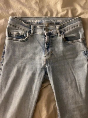 Ljusblåa flare jeans low waist - Snygga ljusblå jeans med låg midja och utsvängda ben. Modellen är flare och har råa kanter nertill för en trendig look. Jeansen har klassiska fem fickor och dragkedja med knapp. Perfekta för dig som gillar retrostil.