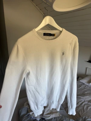 Vit tröja från Polo Ralph Lauren - Klassisk vit tröja från Polo Ralph Lauren med rund halsringning och diskret broderad logga på bröstet. Tröjan är långärmad och har ribbade muddar vid ärmslut och nederkant. Perfekt för en clean och stilren look. Priset är inte hugget i sten, hör av er vid funderingar!