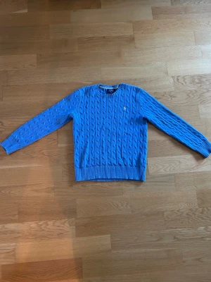 Blå kabelstickad tröja Polo Ralph Lauren - Snygg blå kabelstickad tröja från Polo Ralph lauren. Den har en QR länk som bevisar att varan är äkta. storlek 14-16 år/164-170cm. Bra tröja för sommaren och vintern.