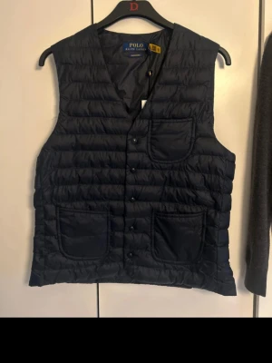 Mörkblå dunväst från Polo Ralph Lauren - Tjena säljer denna Jätte snygga Ralph Lauren väst i quiltad design och tre fickor framtill och Knappar ifrån Volt magasin, jag säljer denna då jag hittade fram den Under min Garderobs rensing av Vinter kläder, den är aldrig använd eftersom den var för liten när jag fick den🌟 finns Qr kod som går direkt till Hemsidan för att ledgit cheka ✅ :Storlek S 📏 Nypris ungefär 4,000