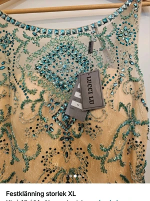 Beige och turkos festklänning Lucci Lu - Superfin långklänning från Lucci Lu i beige med turkosa och silvriga paljetter och pärlor. Klänningen har ärmlös design, djup v-ringning i ryggen och vackra broderade detaljer. Perfekt för bal eller festliga tillfällen.