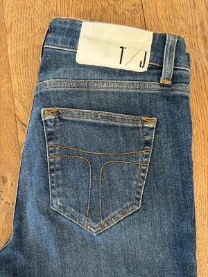 Blå jeans Tiger of Sweden 26/32 - Snygga blå jeans från Tiger of Sweden i modellen Slight. Klassisk femficksdesign med orangea kontrastsömmar och bälteshällor. Perfekta för dig som gillar en stilren och tidlös look. 