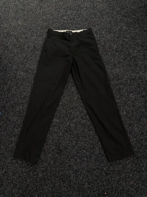 Svarta kostymbyxor från Jack & Jones - Snygga svarta kostymbyxor  från Jack & Jones med loose fit. Klassisk design med raka ben och knappgylf. Tillverkade i mjukt bomullstyg för en bekväm känsla. Perfekta för dig som gillar en avslappnad men stilren look.