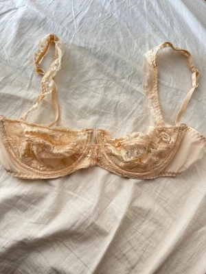 Beige spets-bh med bygel - Säljer en romantisk beige bh med bygel och tunna axelband. Bh:n är dekorerad med vacker spets och har transparenta partier som ger en feminin känsla. Perfekt för dig som gillar detaljer och mjuka material.