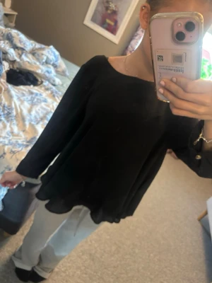 Svart vid blus med guldknappar - Säljer en svart, lös och flowy blus med rund halsringning och långa ärmar. Ärmarna har dekorativa guldknappar vid mudden och materialet känns lätt och luftigt, perfekt för en stilren look. Passar till både jeans och kjol.