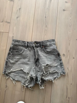 Gråa jeansshorts - Säljer ett par gråa jeansshorts med slitna kanter och fransar. Shortsen har klassisk femficksdesign och dragkedja med knapp. Perfekta för en avslappnad och trendig look.