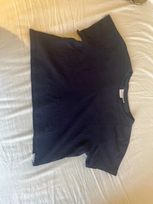 Mörkblå baby tee  - En enkel och stilren mörkblå baby tee i mjuk bomull. T-shirten har korta ärmar, rund halsringning och en rak passform. Perfekt att matcha med jeans eller shorts för en avslappnad look.