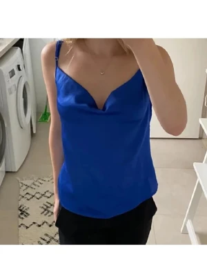 Marinblått satin linne - Säljer ett mörkblått linne med smala justerbara axelband och snygg draperad urringning. Perfekt för att lyfta en outfit med sin glansiga finish och stilrena look. Dubbelt tyg vid bysten. Använd ca 2 ggr.