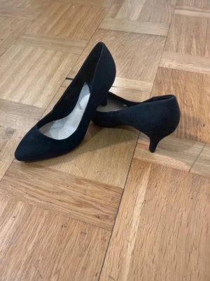 Svarta klackskor från H&M med låg klack - Stilrena svarta klackskor från H&M med spetsig tå och låg klack. Skorna är tillverkade i ett mockaliknande material som ger en mjuk känsla och elegant look. Perfekta för dig som vill ha en klassisk och enkel sko med modern touch.