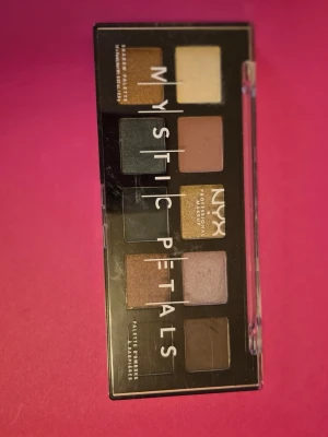 NYX Mystic Petals ögonskuggspalett - NYX Mystic Petals ögonskuggspalett med 10 nyanser i både matta och skimrande färger. Paletten innehåller bland annat guld, grön, blå, brun, lila och beige toner. Perfekt för att skapa kreativa och färgstarka ögonmakeuper. Kommer i en smidig plastförpackning. 3-4 stycken ögonskuggor är swatcchade. Testade för o se färgen.