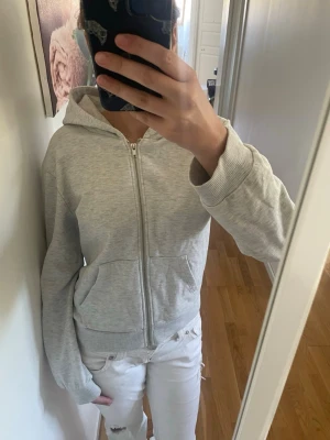 Ljusgrå zip-hoodie med huva - Snygg ljusgrå hoodie med dragkedja och huva. Modellen har två stora fickor framtill och ribbade muddar vid ärmslut och nederkant. Perfekt för en avslappnad och stilren look. Passar till det mesta och är superbekväm.