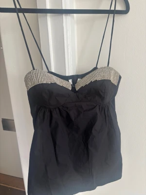 Svart linnetopp med strassdetaljer Zara - Snygg svart linnetopp med tunna axelband och glittrande strass längs bysten. Toppen har en feminin passform och är perfekt för att sticka ut. Materialet känns lätt och smidigt, och toppen har en croppad look. Virala Zara topp helt ny med ettiket helt slutsåld med etikett 