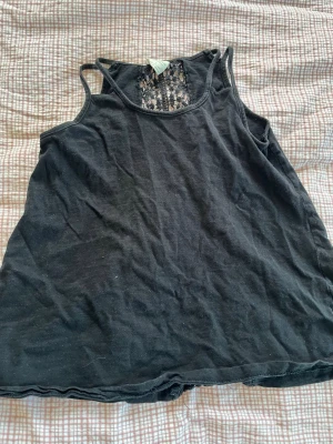 Svart linne med spetsdetalj - Svart linne med smala axelband och snygg spetsdetalj i ryggen. Perfekt för dig som gillar en enkel men ändå unik look. Linnet har en lös passform och är tillverkat i mjukt material som känns skönt mot huden. Linnet är ifrån Zara och i storlek i storlek 7. 