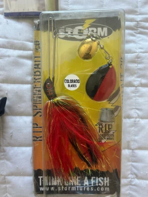 Storm Rip Spinnerbait Colorado - Färgglad spinnerbait från Storm med Colorado-blad i guld och svart/rött. Utrustad med långa röda, svarta och guldiga syntettrådar. Perfekt för fiske efter rovfisk. Förpackningen är genomskinlig och visar betet tydligt.