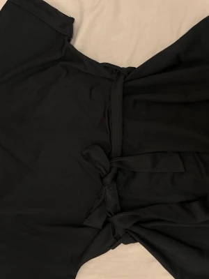 Svart omlotttröja med knytband - Stilren svart omlotttröja med korta ärmar och knytband i midjan. Tröjan har en enkel och klassisk design som passar perfekt till många tillfällen. Tillverkad i mjukt tyg för en bekväm känsla.