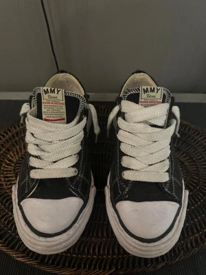 Svarta MMY låga sneakers - Säljer ett par svarta låga sneakers från MMY med vita tjocka snören och vit sula. Skorna har kontrasterande vita sömmar och en klassisk rund tå. Ovandelen är i tyg och sulan är i gummi. Perfekta för en avslappnad streetwear-look.