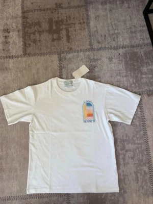 Vit Casa Blanca t-shirt med tryck size s - Säljer en vit t-shirt från Casa Blanca med färgglatt grafiskt tryck fram och bak i blått, orange och gult. T-shirten har rund hals och korta ärmar. Perfekt för dig som gillar stilrena plagg med en twist.