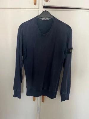 Mörkblå tröja från Stone Island äkta  - Snygg mörkblå långärmad tröja från Stone Island med rund halsringning och ikonisk logopatch på vänster ärm. Tröjan har ribbade muddar vid ärmslut och nederkant. Perfekt för en avslappnad och stilren look.