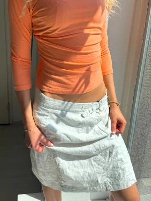 Vit linnekjol med fickor - Säljer en vit kjol i linne med normal passform och praktiska fickor framtill. Kjolen har en enkel och stilren design som passar perfekt till sommaren. Midjelinningen har en liten detalj med knapp och kjolen slutar strax ovanför knäna.