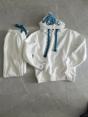 Vita mjukisbyxor med blå snören - Snygga vita mjukisbyxor med elastisk midja och blå dragsko. Byxorna har en relaxed fit och är tillverkade i mjukt material, perfekta för chill dagar. Liten blå brodyr vid benet ger extra stilpoäng.