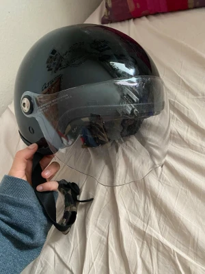 Motorcykel/scooter hjälm - Justerbart hakband. Insidan har ett vadderat foder i camouflagemönster för extra komfort. Perfekt för dig som vill ha både stil och skydd när du kör moped eller scooter.