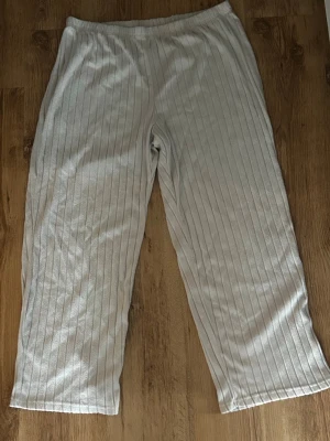 Grå ribbade loungebyxor - Mysiga loungebyxor i beige med ribbad struktur och raka ben. Byxorna har resår i midjan för extra komfort och är tillverkade i ett mjukt, stretchigt material som passar perfekt för hemmakvällar eller chill dagar.