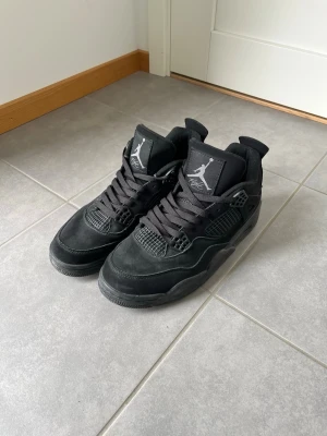 Svarta Air Jordan 4 sneakers - Säljer ett par helsvarta Air Jordan 4 sneakers med klassisk siluett och Jumpman-logga på plösen. Skorna har ovandel i mocka och meshdetaljer samt svarta skosnören. Perfekta för dig som gillar streetwear och vill ha en ikonisk look.