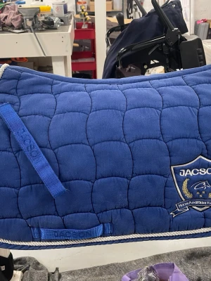 Blått schabrak från Jacson - Säljer ett blått schabrak från Jacson! Bra skick inte sönder på något ställe. Använt 7 gånger ish. Inte smutsigt men pytte lite hårigt på kardborrebandet där man sätter fast stropparna i.💙 ny pris är 650kr