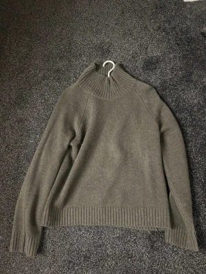 Olivgrön stickad polo tröja från Wera - Snygg olivgrön stickad tröja från Wera med hög, ribbad polokrage och långa ärmar. Tröjan har ribbade muddar vid ärmslut och nederkant, vilket ger en clean och modern look. Perfekt för lager på lager under kyliga dagar. Helt ny