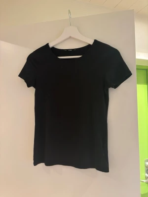 Svart basic t-shirt i bomull - En enkel svart t-shirt med rund hals och korta ärmar. Tillverkad i mjuk bomull, perfekt för en clean och stilren look. Passar till allt och är ett måste i garderoben.