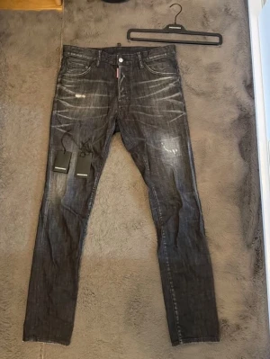 Svarta Dsquared2 jeans med slitningar - Säljer ett par svarta jeans från Dsquared2 med coola slitningar och tvättade detaljer.klassiska fem fickor och en röd Dsquared2-logga vid fickan. Perfekta för dig som gillar streetwear och vill sticka ut. Inte använda mycket. Nypris 5899. Mitt pris 2999. (Kan diskuteras vid smidig affär) 