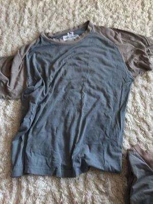 Gråblå t-shirt från Kriminalvården - Unisex t-shirt i gråblå färg med ljusgrå kontrastfärg på ärmar och krage. Tillverkad för Kriminalvården av Arbetsskydd Express. Materialet är 65% bomull och 35% polyester, vilket gör den mjuk och bekväm. Klassisk passform och korta ärmar. 500 för båda
