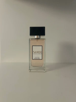 Noir Eau de Toilette från Hunkemöller - Noir Eau de Toilette från Hunkemöller i en elegant, rektangulär glasflaska med svart lock. Doften har en ljus, nästan transparent färg och etiketten är stilren med svart text. Perfekt för dig som gillar exklusiva och moderna parfymer.