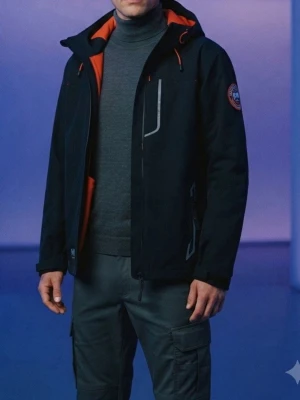 Svart fleecejacka från Helly Hansen - Snygg svart fleecejacka från Helly Hansen med orange detaljer och huva. Jackan har dragkedjor framtill, två sidofickor och en bröstficka med reflekterande detaljer. Märkespatch på ärmen och justerbar huva. Perfekt för blåsiga dagar.