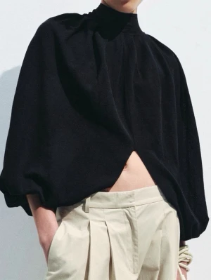 Svart polotopp med öppen rygg flowy tröja - Unik svart polotopp med voluminösa ärmar och öppen rygg. Toppen har en lös passform och ballongärmar som ger en cool siluett. Perfekt för dig som vill sticka ut med en edgy och modern look.
